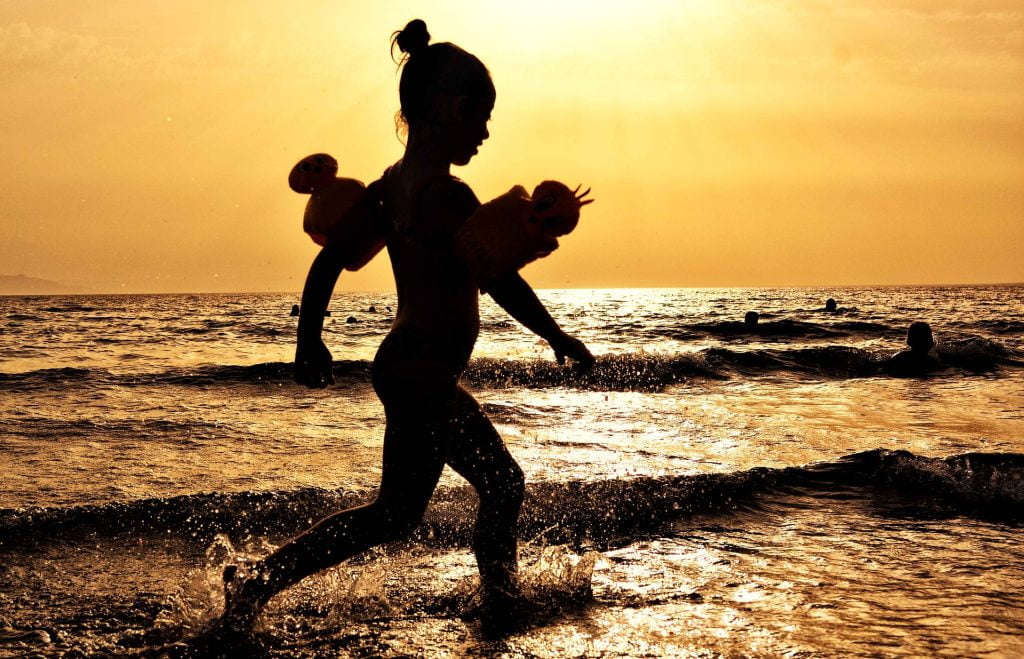 Niña con flotadores corriendo cerca de la playa